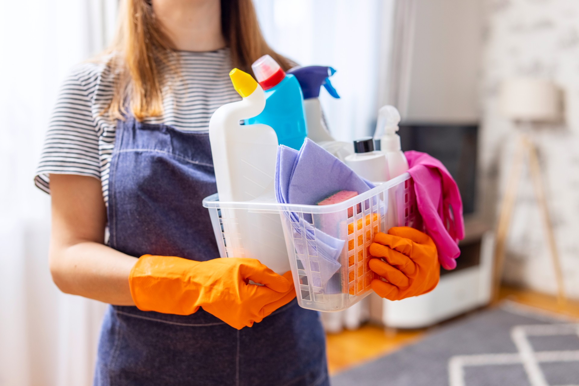 Woman in rubber gloves with basket of cleaning supplies ready to clean up